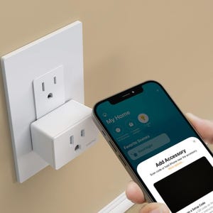 A smartphone displaying a smart home app and a smart plug inserted into a wall outlet.