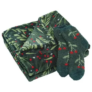 A folded blanket and a pair of socks with a festive green and red holly pattern.