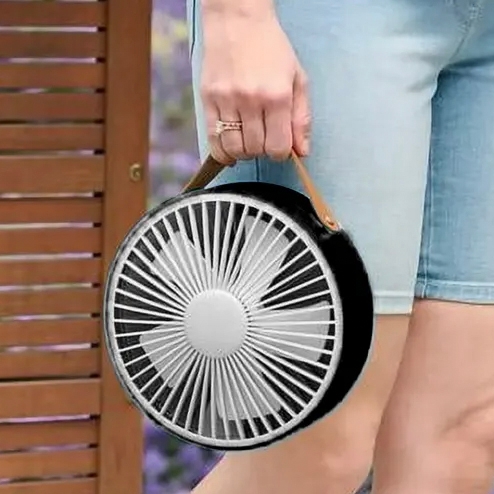 A person is carrying a portable, round fan with a handle, designed for easy transport.