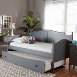 Gray daybed with a trundle in a cozy room with a rug, side table, potted plant, and decorative pillows.