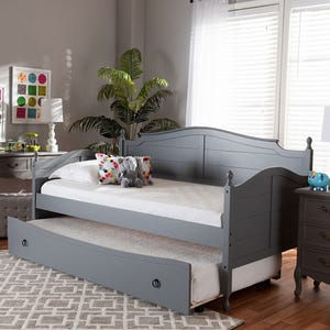 Gray daybed with a trundle in a cozy room with a rug, side table, potted plant, and decorative pillows.