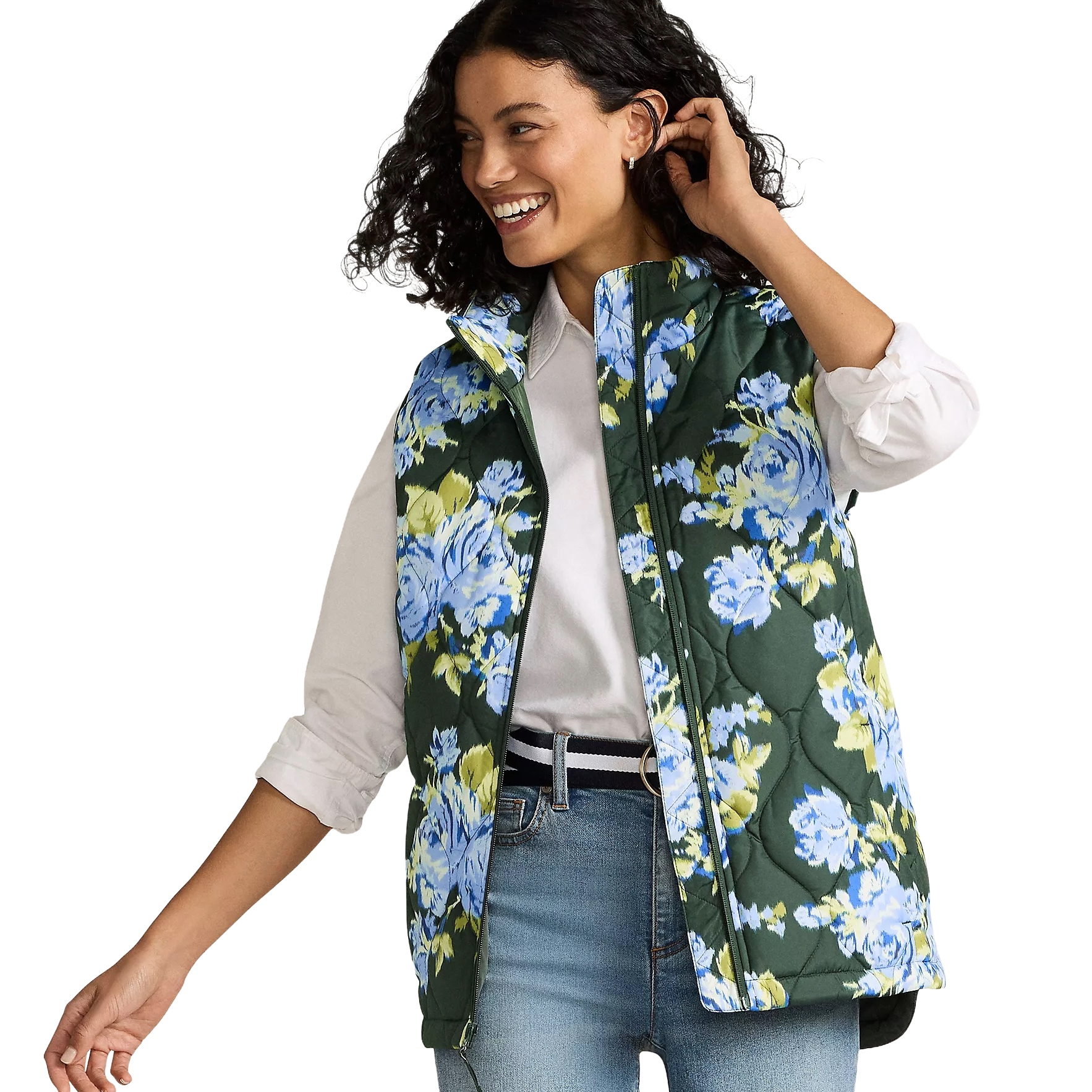 A woman wears a sleeveless quilted vest with a green base and blue floral pattern, paired with a white shirt and blue jeans.
