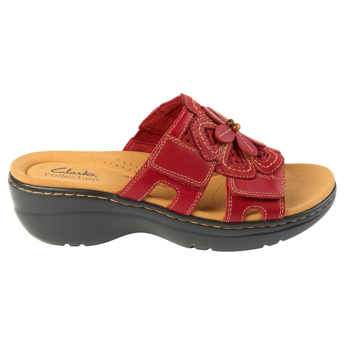 Clarks Merliah Belle Wedge Sandal is a red slip-on sandal with decorative floral accents, featuring a comfortable cushioned footbed and a black wedge sole.