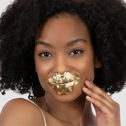 A woman wears a gold lip mask shaped like large lips focused on moisturizing and plumping.