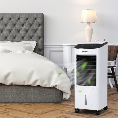 Portable air cooler next to a bed with a grey headboard, white bedding, and a nightstand with a lamp.