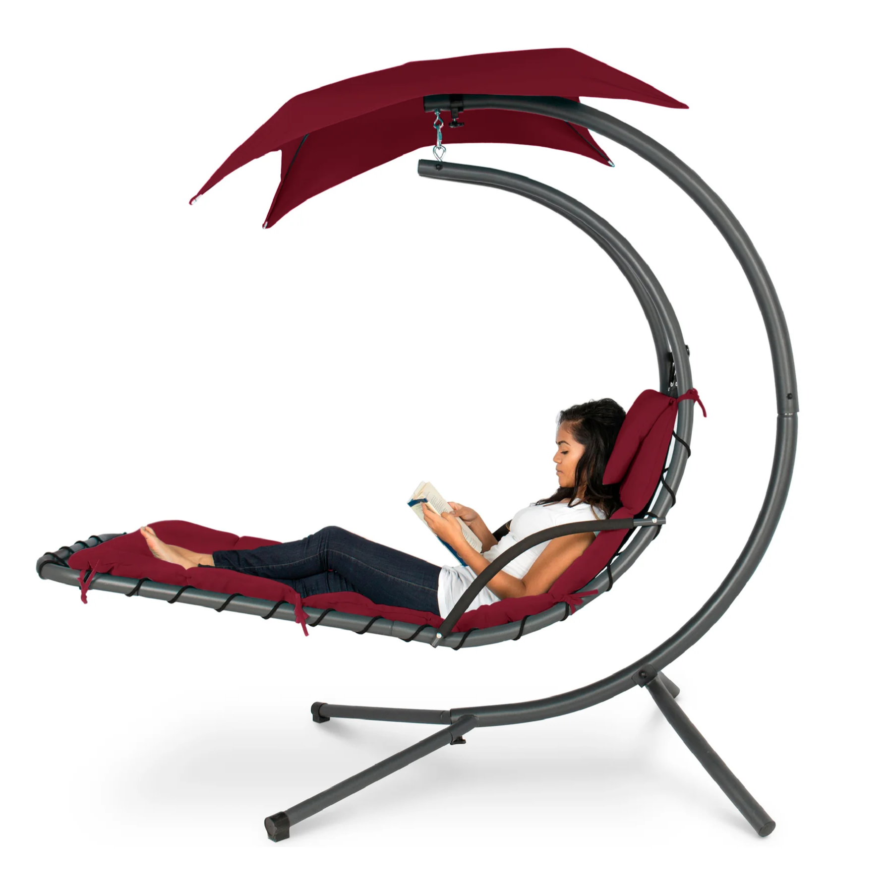 A woman is reading on a hanging lounge chair with a red cushion and canopy, supported by a curved gray frame.