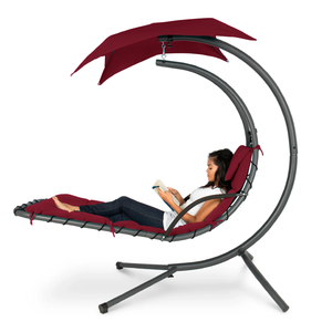 A woman is reading on a hanging lounge chair with a red cushion and canopy, supported by a curved gray frame.