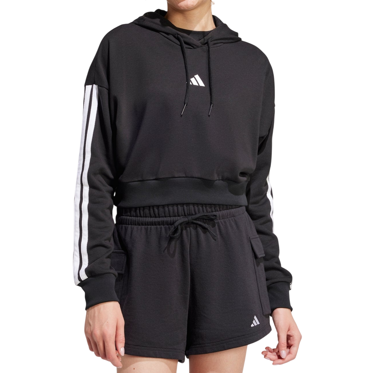 A person wears a black Adidas hoodie with white stripes on the sleeves and black shorts featuring the Adidas logo.