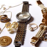 A collection of gold-toned jewelry including a wristwatch, bracelets, earrings, and rings, with pearl and gemstone accents.