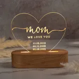 Heart-shaped LED night light with \“mom, we love you\“ text and three date engravings: 12.09.2012, 05.11.2008, 03.06.2001, mounted on a wooden base.