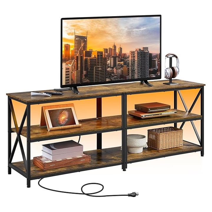 A rustic TV stand with open shelving, featuring a wood and metal design, holding a flat-screen TV, headphones, and other accessories. It includes integrated power outlets for convenient device charging.