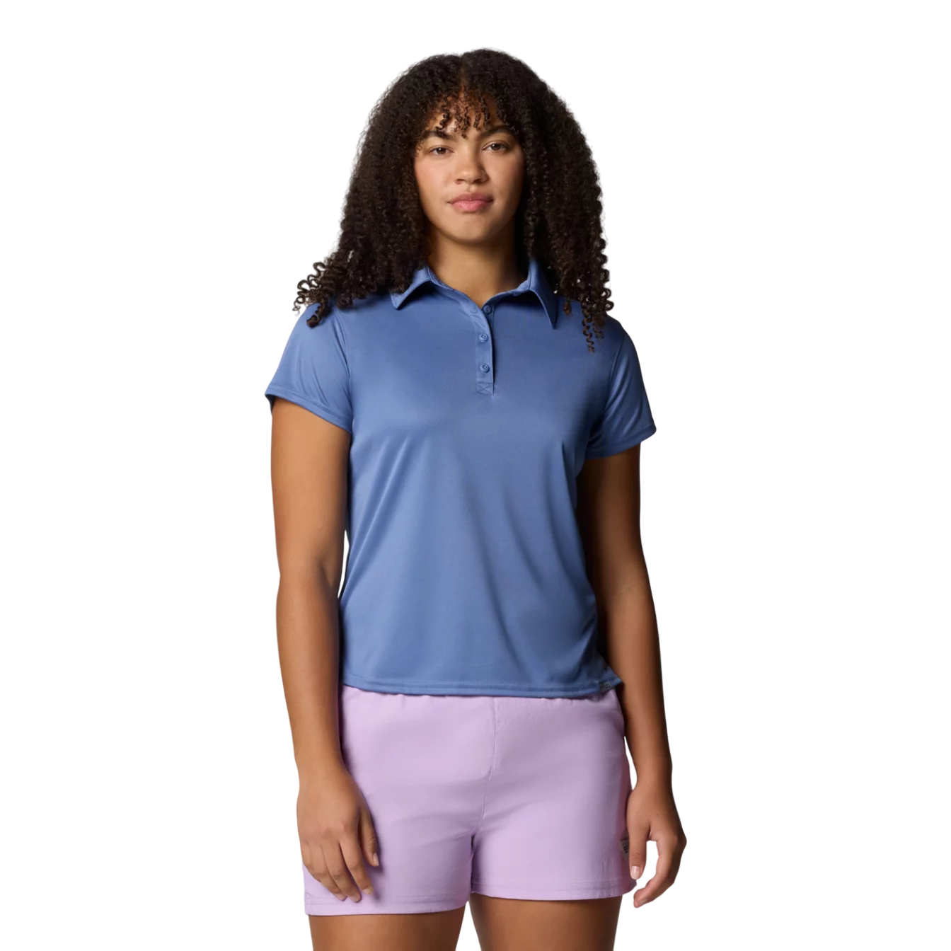 A woman is wearing a blue short-sleeve polo shirt and light purple shorts, standing against a plain background.
