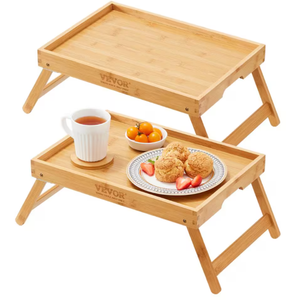 Two bamboo bed trays with foldable legs, one holding a cup of tea and a plate of cookies and fruit.