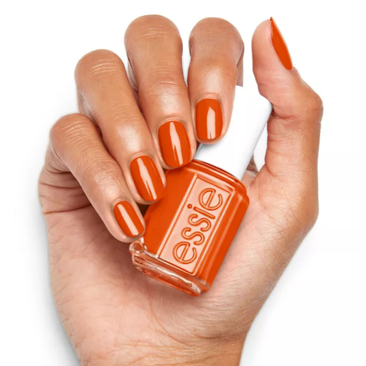 An orange nail polish bottle from Essie held in a hand with matching polished nails.