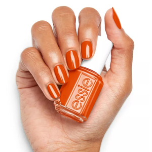 An orange nail polish bottle from Essie held in a hand with matching polished nails.
