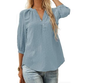 Light blue, long-sleeve blouse with a Swiss dot pattern, featuring a Henley neckline and button detail. Paired with blue jeans.