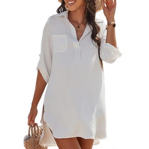 White long-sleeve shirt dress with a collar and chest pocket, styled with rolled-up sleeves. The person is also wearing a brown bracelet and carrying a woven straw handbag.
