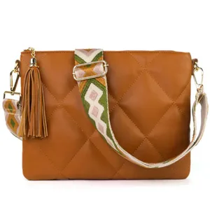 Tan quilted crossbody bag with a geometric-patterned strap and a tassel accent.