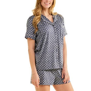 A woman is wearing a short-sleeved, button-up pajama set with a navy blue and white circular pattern, consisting of a top and matching shorts.
