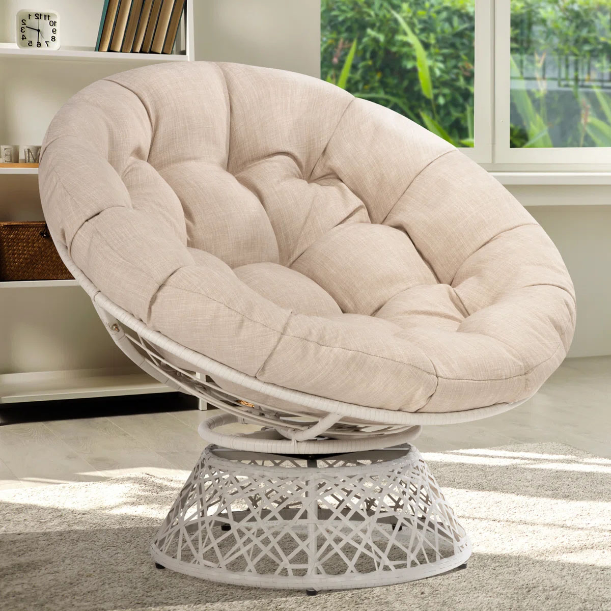 Beige tufted papasan chair with a metal base, placed in a bright room with bookshelves and windows in the background.