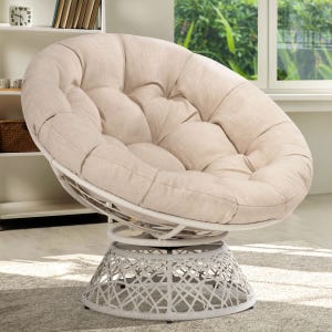 Beige tufted papasan chair with a metal base, placed in a bright room with bookshelves and windows in the background.