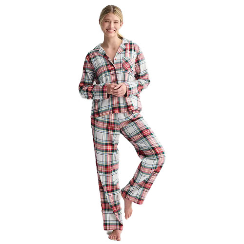 A person wearing a plaid pajama set featuring a button-up long-sleeve top and matching pants with a red, black, and white checker pattern.