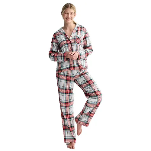 A person wearing a plaid pajama set featuring a button-up long-sleeve top and matching pants with a red, black, and white checker pattern.