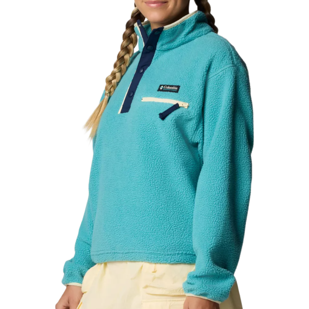 A person is wearing a turquoise Columbia fleece pullover with a navy button placket and a zippered chest pocket, paired with light-colored pants.