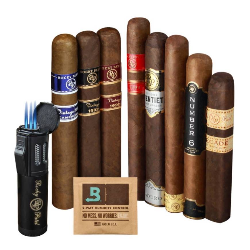 The photo shows a collection of cigars with various labels, a torch lighter, and a humidity control packet.