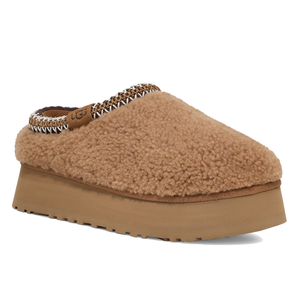 A tan slip-on mule with a fluffy, shearling-like texture, featuring a raised platform sole and decorative stitching around the ankle, from UGG.