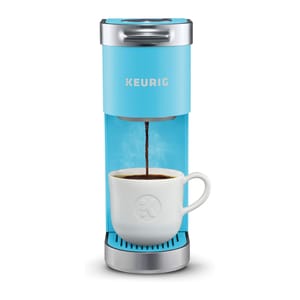 A light blue Keurig single-serve coffee maker with a white mug underneath, brewing coffee.