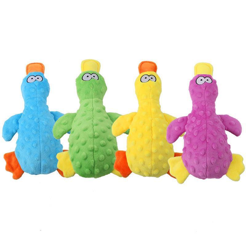 Four colorful squeaky duck dog toys are shown in blue, green, yellow, and purple. Each duck has a textured surface, cartoonish eyes, orange feet, and brightly colored beaks, with variations between orange and yellow.