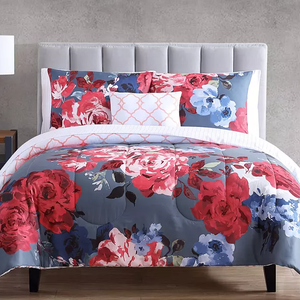A bed with a gray upholstered headboard features floral bedding with red, pink, and blue flowers on a dark background, accompanied by a white and coral accent pillow.
