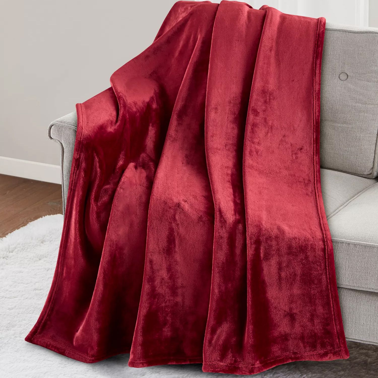A red velvet blanket draped over a light gray sofa, with a white rug on the wooden floor beneath.