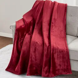 A red velvet blanket draped over a light gray sofa, with a white rug on the wooden floor beneath.