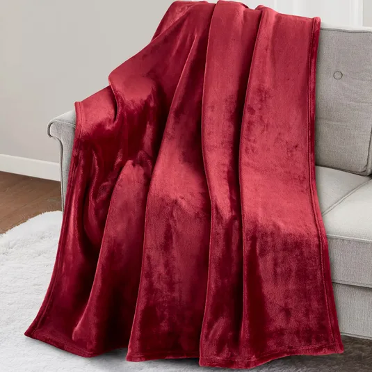 A red velvet blanket draped over a light gray sofa, with a white rug on the wooden floor beneath.