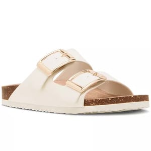 A white slide sandal with two gold buckle straps and a cork footbed.