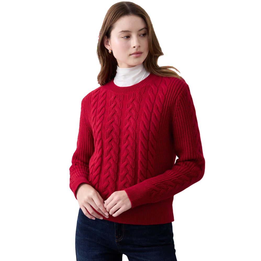 A woman is wearing a red cable-knit sweater with a white turtleneck underneath, paired with dark blue jeans.
