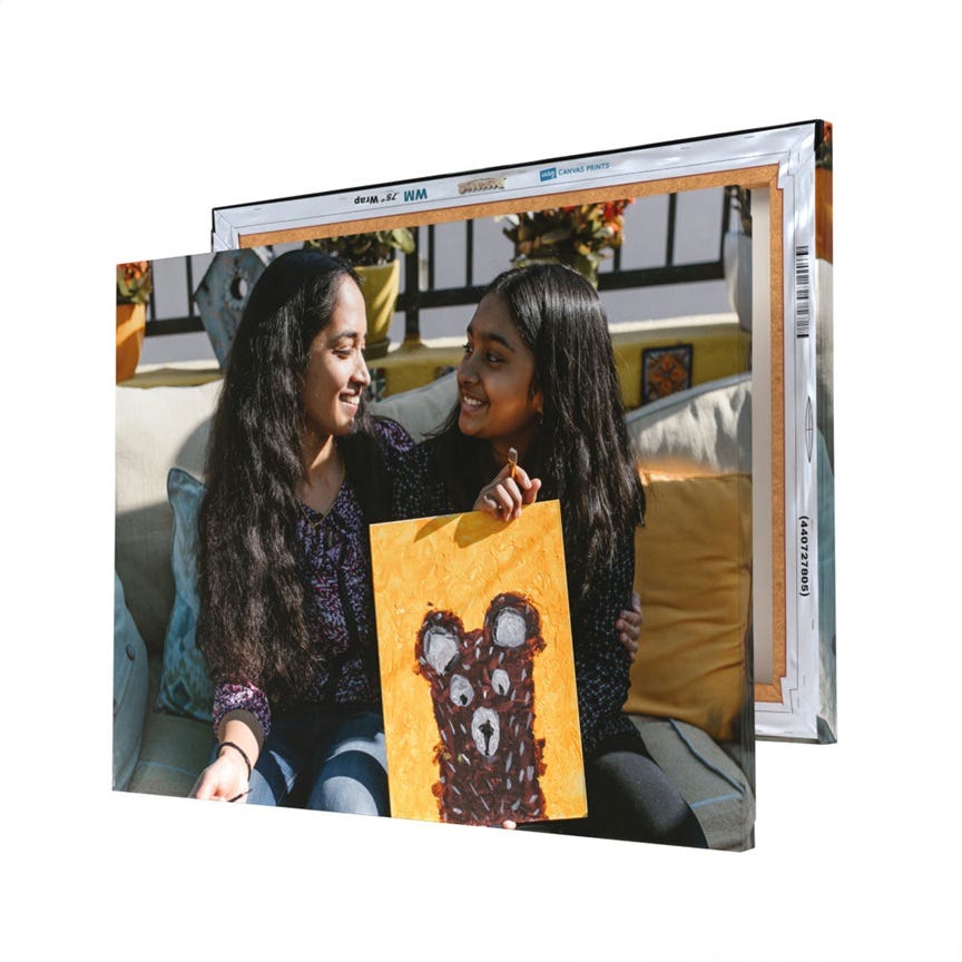 Two canvas prints are displayed, with one showing two people sitting together holding a painting of a bear with a yellow background.