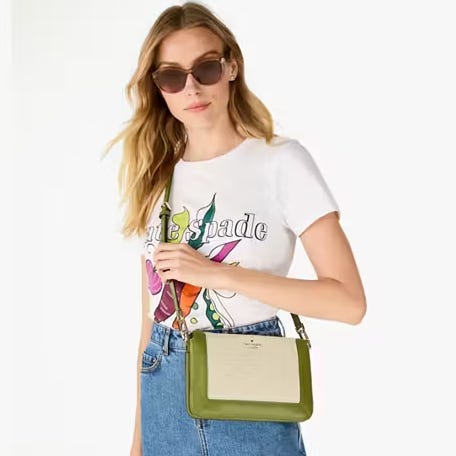 A woman wearing a white T-shirt with colorful print, sunglasses, denim jeans, and carrying a small green crossbody bag.