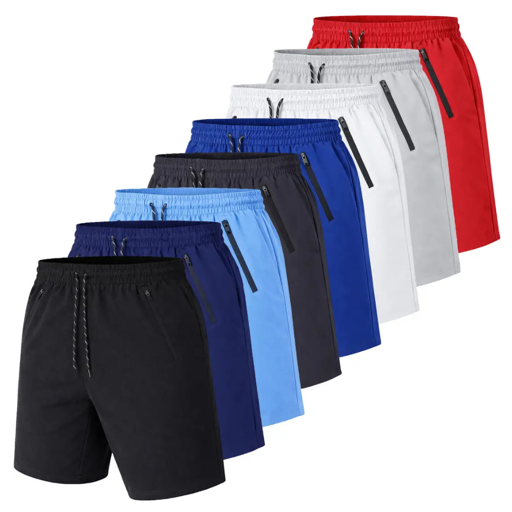 A collection of athletic shorts in various colors, including black, dark blue, light blue, navy, gray, white, and red, each with zippered pockets and an elastic waistband with a drawstring.
