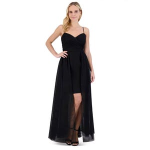 A woman is wearing a black evening gown with a fitted bodice and spaghetti straps, featuring a sheer overlay skirt.