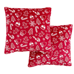 Two red throw pillows with white holiday-themed patterns, including gingerbread men, candy canes, snowflakes, trees, mittens, and bells.