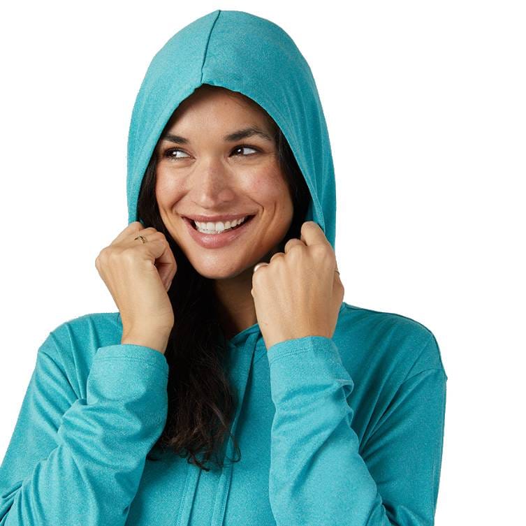 A person wearing a teal hooded sweatshirt is smiling and holding the hood with both hands.