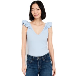 A woman is wearing a light blue sleeveless top with ruffled shoulders and V-neck, paired with dark blue jeans.