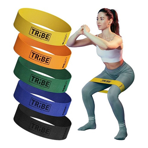 A woman exercising with one of the multiple colorful resistance bands stacked next to her.