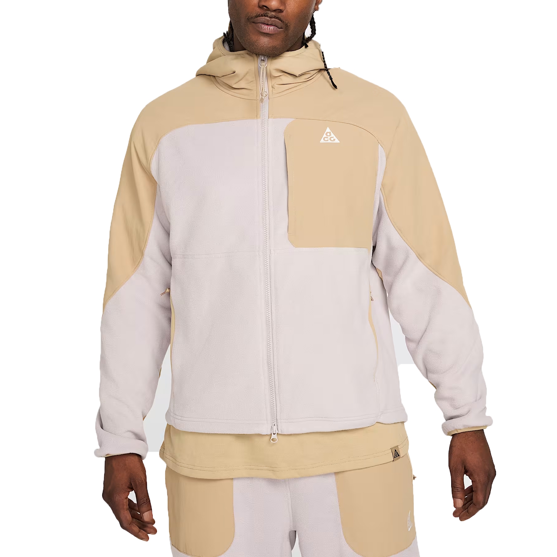 A hooded jacket with a color-block design in beige and light grey, featuring a full zip front and a chest pocket with a small triangular logo. It is paired with matching pants that have similar color blocking.