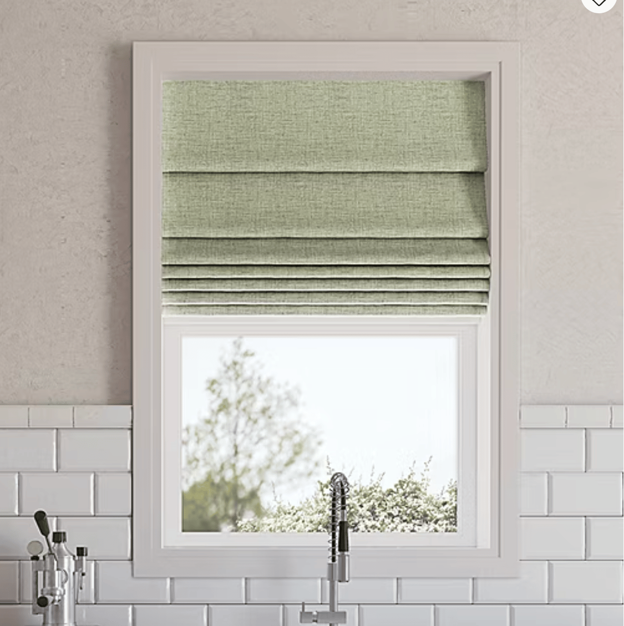 A kitchen window features light green Roman shades partially drawn, above a sleek, modern faucet. The wall is lined with white subway tiles.
