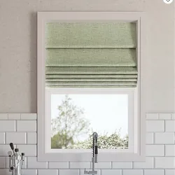 A kitchen window features light green Roman shades partially drawn, above a sleek, modern faucet. The wall is lined with white subway tiles.