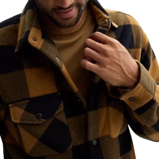 A warm, snap-front shirt jacket with a black and mustard plaid pattern, featuring a rugged, textured fabric and flap pockets on the chest for a classic, cozy look.